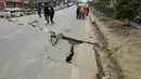 Sejumlah warga di Kathmandu berjalan melintasi jalan yang rusak akibat gempa , Minggu (26/4/2015). Gempa berkekuatan 7,8 Skala Richter dikabarkan telah menelan korban sekitar 2000 jiwa. (AFP Photo/Prakash Mathema)