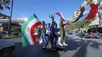 Pendukung pemerintah mengibarkan bendera Suriah, Iran, dan Rusia saat berdemonstrasi di Damaskus, Suriah, 14 April 2018. Suriah tengah mengalami gejolak krisis ekonomi dengan nilai tukar mata uang yang merosot dalam beberapa hari terakhir. (AP Photo/Hassan Ammar, File)