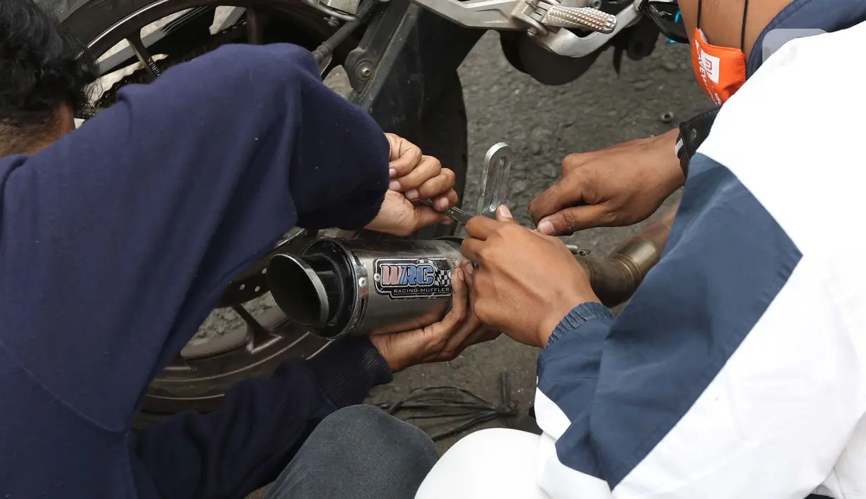 Pengendara motor mencopot knalpot bising usai terjaring razia yang digelar Satlantas Polres Metro Depok di Jalan Margonda Raya, Depok, Kamis (18/3/2021). Puluhan motor berknalpot bising yang terjaring razia diwajibkan mengganti knalpot dan diberi sanksi tilang. (Liputan6.com/Helmi Fithriansyah)