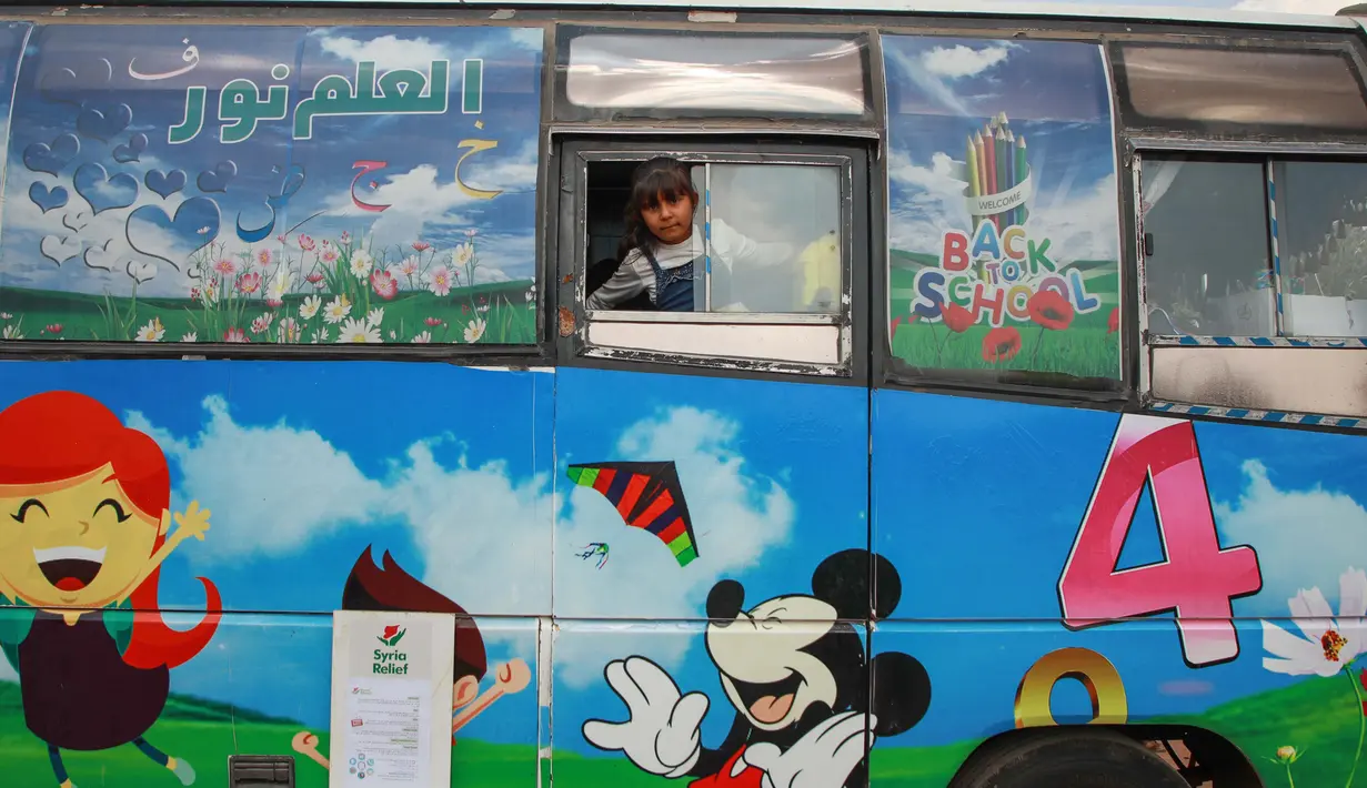 Seorang anak mengintip dari jendela bus yang diubah menjadi ruang kelas di desa Hazano di barat laut Suriah (15/9/2019). Kelas di dalam bus ini hanya melayani usia mulai dari 5 hingga 12 tahun. (AFP Photo/Aaref Watad)