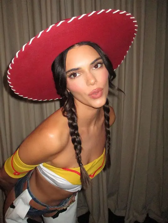 Kendall Jenner memamerkan perutnya yang kencang dalam balutan kemeja putih bergaya kartun dengan kerah besar, kancing, dan detail manset kuning. (Instagram/Kendalljenner)