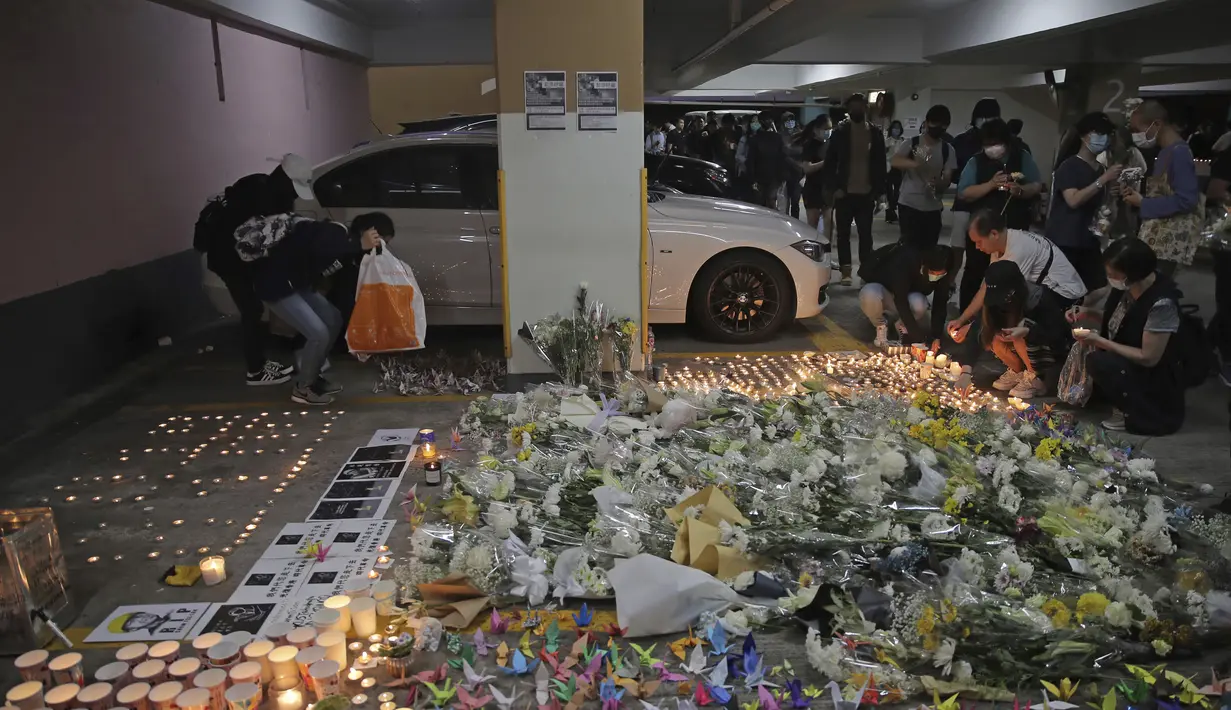 Para pengunjuk rasa menyalakan lilin di dekat bunga-bunga di lokasi tempat mahasiswa Alex Chow Tsz-lok jatuh di Hong Kong (8/11/2019). Chow ditemukan terbaring dengan genangan darah di sebuah tempat parkir mobil, yang menjadi sasaran penembakan gas air mata oleh polisi. (AP Photo/Kin Cheung)