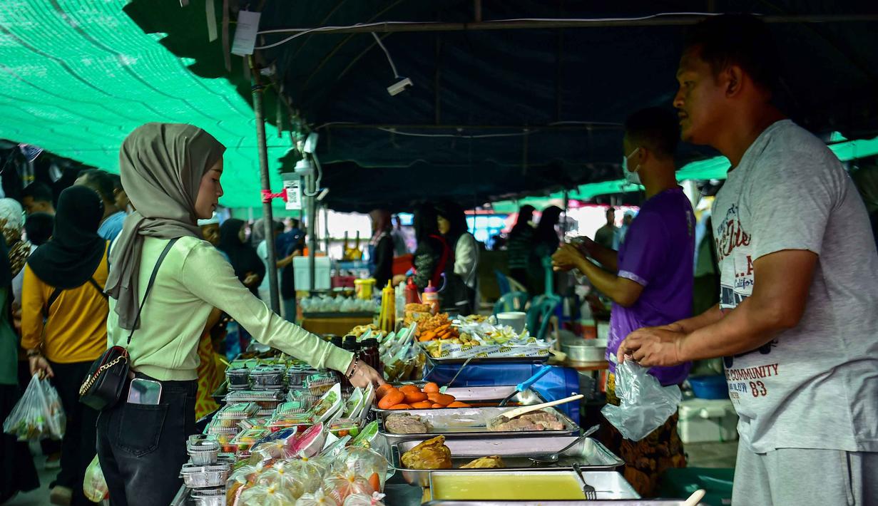 Berbagai jenis kue basah manis seperti tepung pelita dan akok menjadi yang paling dicari warga loka untuk berbuka puasa. Tampak dalam foto, seorang wanita membeli makanan untuk berbuka puasa pada hari pertama bulan suci Ramadan 1447 Hijriah di sebuah pasar di provinsi Narathiwat, Thailand selatan, pada Kamis 19 Februari 2026. (Madaree TOHLALA/AFP)
