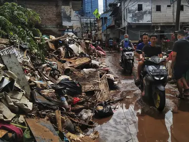Pengendara sepeda motor melintas saat warga membersihkan sampah sisa banjir di Kebalen, Jakarta, Minggu (21/2/2021). Banjir yang terjadi kemarin karena curah hujan yang tinggi meninggalkan sampah di rumah warga. (Liputan6.com/Johan Tallo)