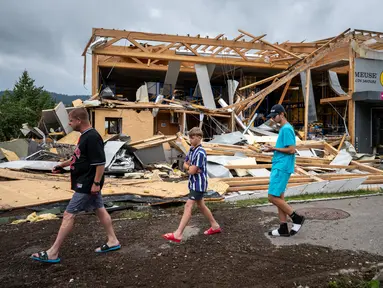 Orang-orang berjalan melewati bangunan yang rusak, beberapa jam setelah badai dahsyat menerjang aera di Le Cret-du-Locle dekat La Chaux-de-Fonds, Swiss barat, Senin (24/7/2023). (Fabrice COFFRINI / AFP)