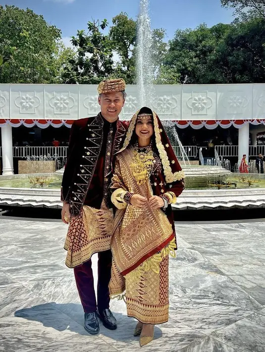 Nirina Zubir dan Ernest kompak mengenakan pakai adat Koto Gadang warna merah maroon keemasan. Baju yang saat keduanya menikah. [Instagram/@nirinazubir_]