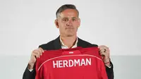 Sebagai informasi, John Herdman datang ke Indonesia dengan membawa sejumlah pengalaman sukses, terutama saat bertugas di Kanada. Dia mengantar timnas putri Kanada meraih dua medali perunggu berturut-turut dalam Olimpiade 2012 dan 2016. Tampak dalam foto, pelatih kepala tim nasional sepak bola Indonesia yang baru, John Herdman memegang jersey tim yang bertuliskan namanya saat konferensi pers di Jakarta, Selasa 13 Januari 2026. (AP Photo/Achmad Ibrahim)