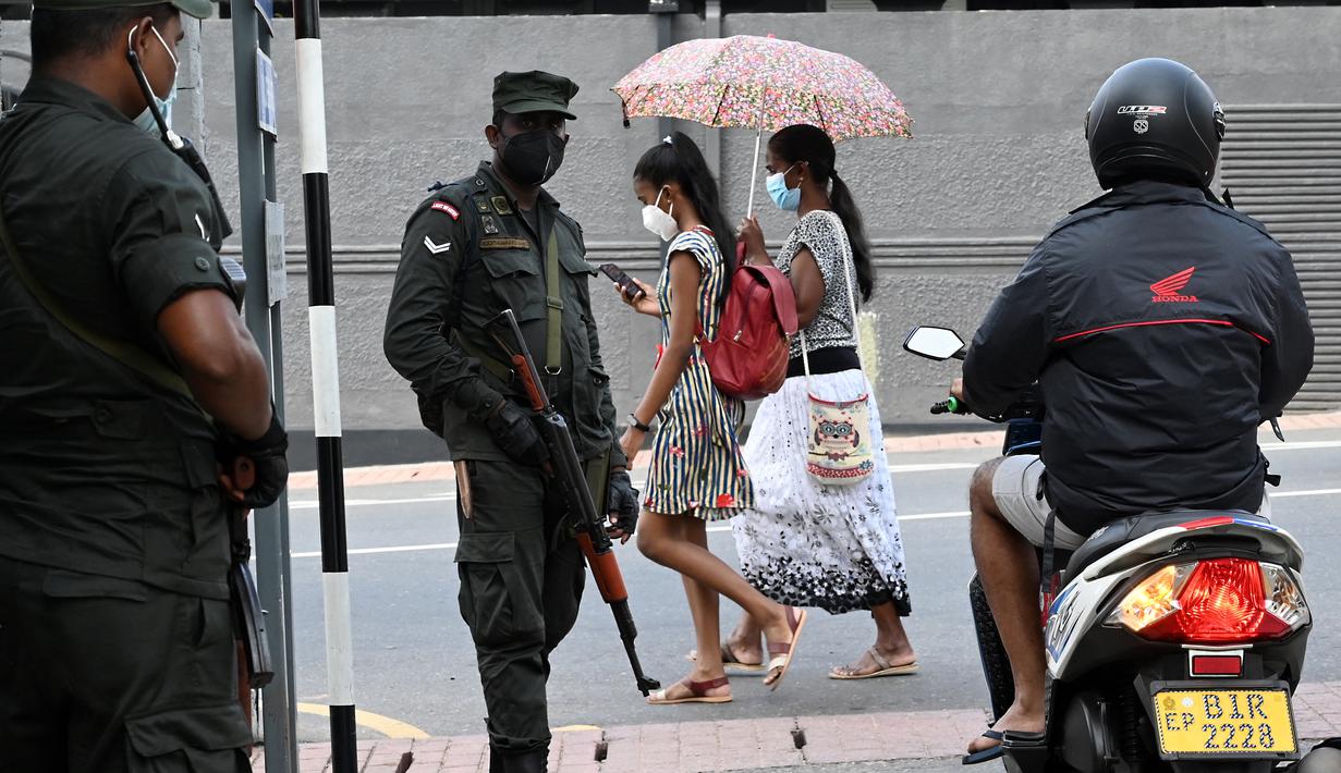 Pejalan kaki melewati tentara yang berjaga di sepanjang jalan di Kolombo pada Sabtu (2/4/2022). Pasukan yang dipersenjatai dengan senapan serbu otomatis dikerahkan di Sri Lanka untuk mengendalikan massa, beberapa jam setelah presiden menyatakan keadaan darurat. (KODIKARA / AFP)