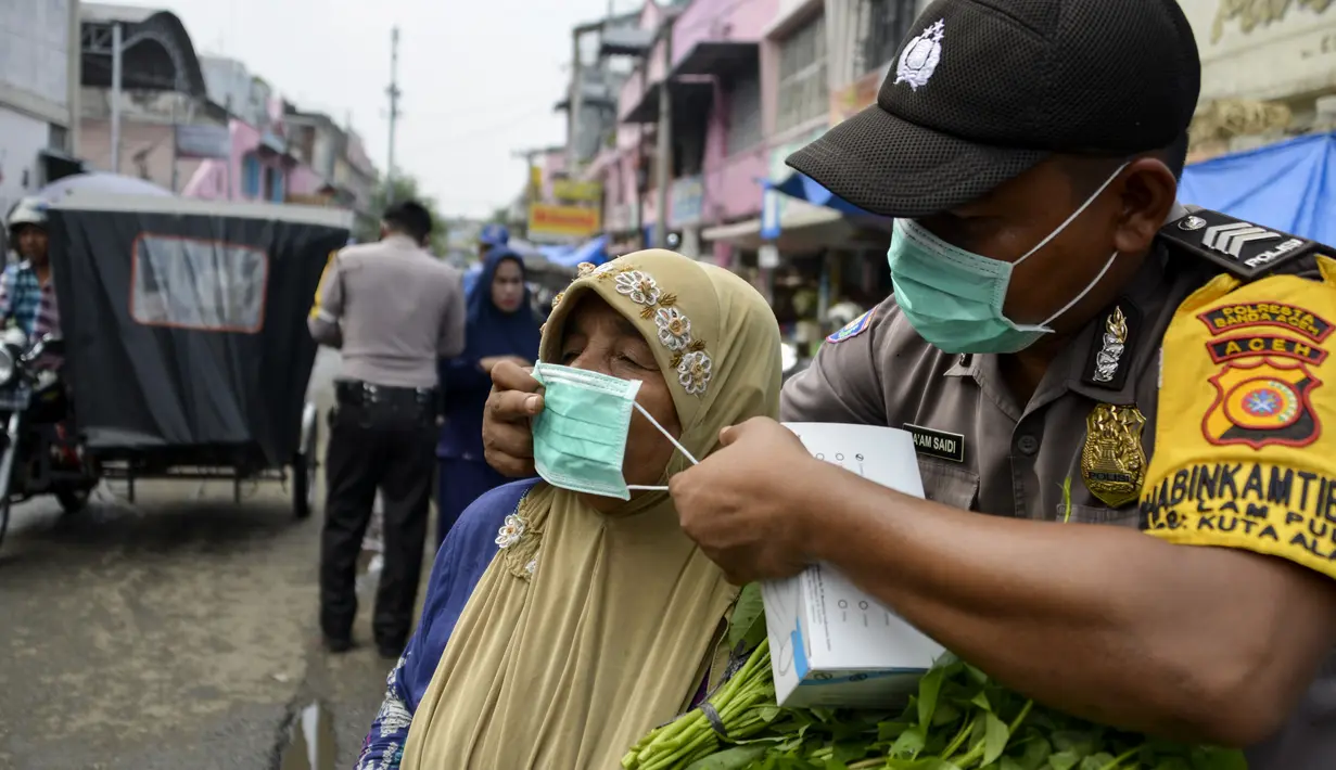 Petugas polisi memasangkan masker kepada warga saat kabut asap tebal menyelimuti wilayah Banda Aceh (25/9/2019). Kebakaran hutan Indonesia menyebabkan hampir 10 juta anak dalam risiko pencemaran udara. (AFP Photo/Chaideer Mahyuddin)