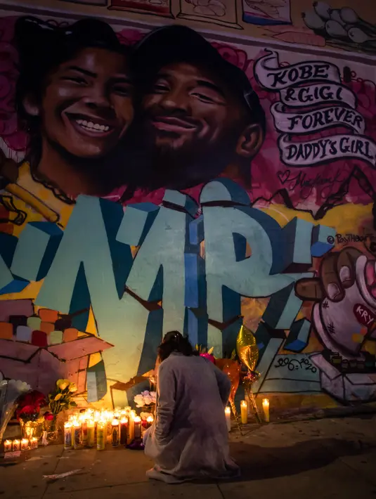 Seorang perempuan meletakkan lilin di depan mural bergambar Kobe Bryant dan putrinya Gianna Bryant di Los Angeles, Senin (27/1/2020). Pemain basket legendaris NBA Kobe Bryant bersama putrinya, Gianna yang berusia 13 tahun meninggal dunia dalam kecelakaan helikopter pada Senin (27/1). (Apu GOMES/AFP)