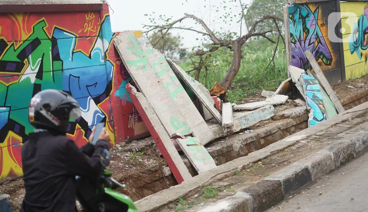 Pengendara motor berhenti dekat tembok Jalan Juanda yang ambruk di kawasan Depok, Jawa Barat, Senin (2/12/2019). Kondisi tembok yang dipenuhi mural tersebut mulai rapuh dan sebagian sisinya telah ambruk serta miring sehingga membahayakan pejalan kaki. (Liputan6.com/Immanuel Antonius)