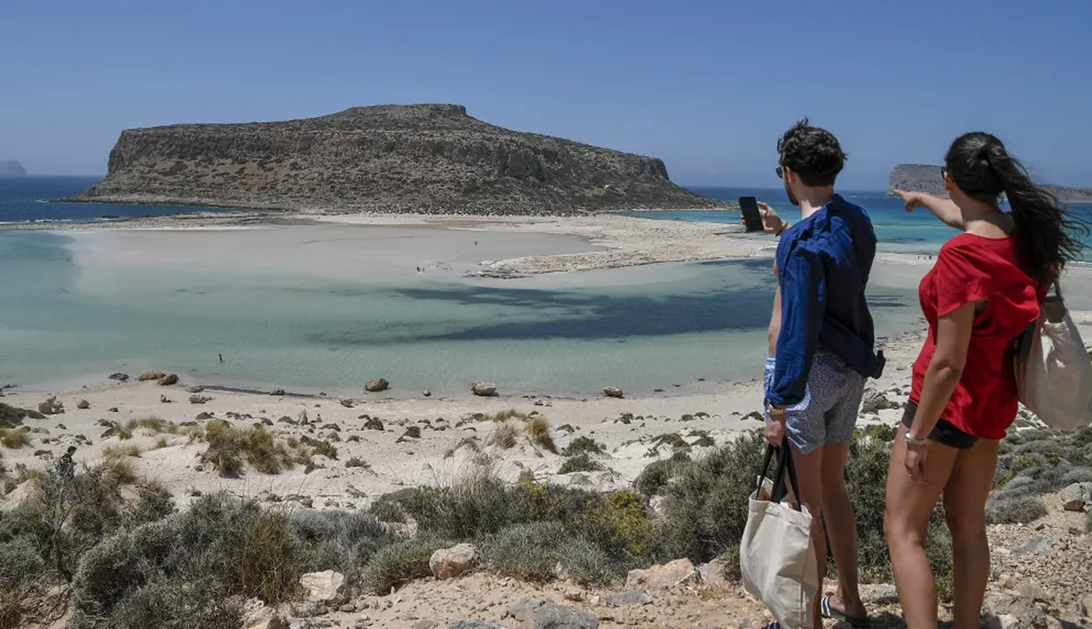 Sepasang wisatawan melihat Pantai Balos dan laguna di barat laut Pulau Kreta, Yunani, Kamis (13/5/2021). Yunani mempermudah langkah-langkah terkait COVID-19 dalam menyambut turis internasional pada 14 Mei. (Louisa GOULIAMAKI/AFP)