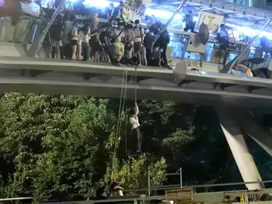 Demonstran menuruni jembatan menggunakan tali untuk melarikan diri dari Universitas Politeknik Hong Kong di Distrik Hung Hom, Hong Kong, Senin (18/11/2019). Lusinan demonstran melarikan diri dari Universitas Politeknik Hong Kong yang dikepung polisi selama berhari-hari. (AP Photo/Kin Cheung)