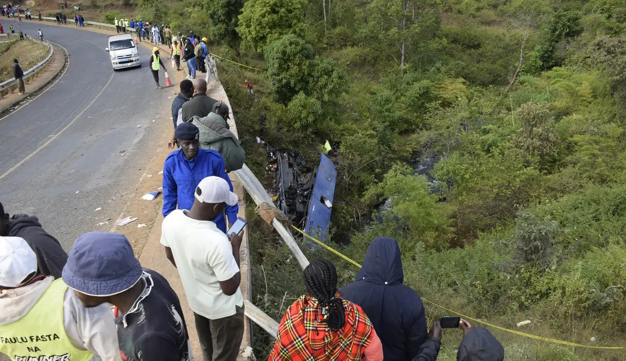 Orang-orang melihat bangkai bus yang jatuh ke jembatan Nithi pada hari Minggu, di Kabupaten Tharaka Nithi, Kenya, Senin (25/7/2022). Penyelidikan awal menunjukkan rem bus blong hingga membuat pengemudinya tak mampu membelokkan kendaraan dengan benar di tikungan tajam di jembatan. (AP Photo/Dennis Dibondo)