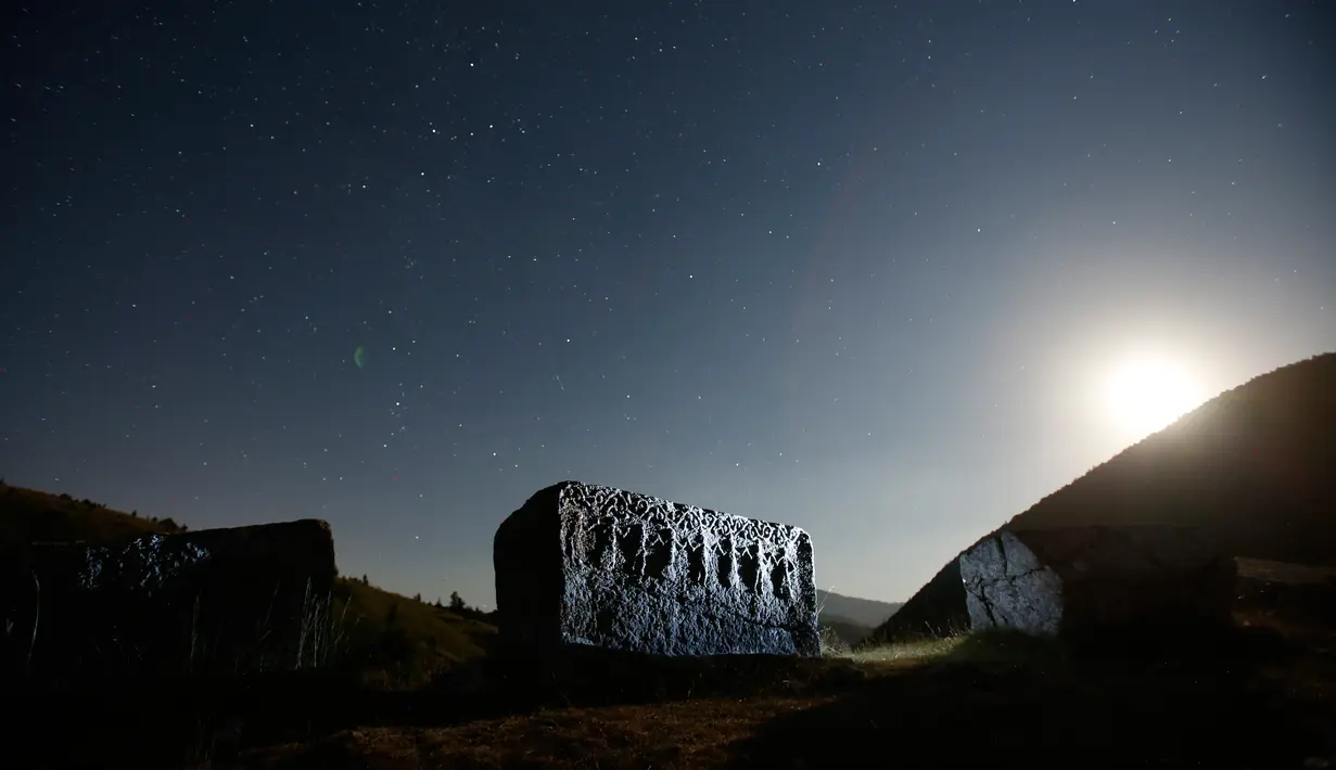 Bintang dan garis-garis meteor (dekat garis cakrawala) terlihat di balik batu nisan abad pertengahan di gunung Bjelasniaca, Bosnia (11/8). Fenomena hujan meteor Perseid terjadi setiap tahun mulai dari Juli sampai akhir Agustus. (AP Photo/Amel Emric)