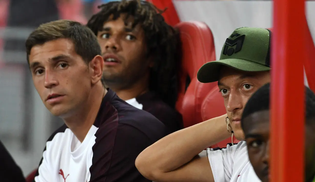 Gelandang Arsenal, Mesut Ozil berada di bangku cadangan saat melihat rekannya bertanding melawan Atletico Madrid di International Champions Cup di Singapura (26/7). Arsenal kalah 3-1 setelah bermain 1-1 di waktu normal. (AFP Photo/Roslan Rahman)