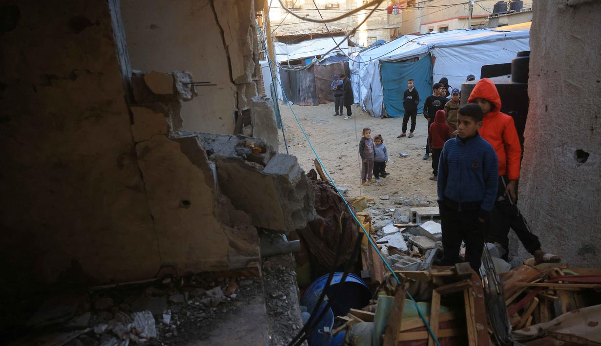 Di sisi lain, pemerintah Gaza juga menyoroti kegagalan pelaksanaan komitmen kemanusiaan dalam kesepakatan gencatan senjata. Dari 57.000 truk bantuan yang seharusnya masuk selama fase pertama, hanya 24.611 truk yang benar-benar diizinkan masuk ke Gaza. Tampak dalam foto, anak-anak Palestina memeriksa rumah yang hancur setelah serangan militer Israel terhadap rumah keluarga al-Houli, di mana empat orang dilaporkan tewas, di sebelah barat Deir al-Balah, di Jalur Gaza tengah pada Jumat 16 Januari 2026. (BASHAR TALEB/AFP)