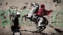 Seorang pria berjalan melewati mural yang diduga karya seniman sekaligus aktivis Banksy di Paris, Prancis, Minggu (24/6). Banksy menyoroti kebijakan pemerintah yang menomorduakan pencari suaka di Eropa. (PHILIPPE LOPEZ/AFP)