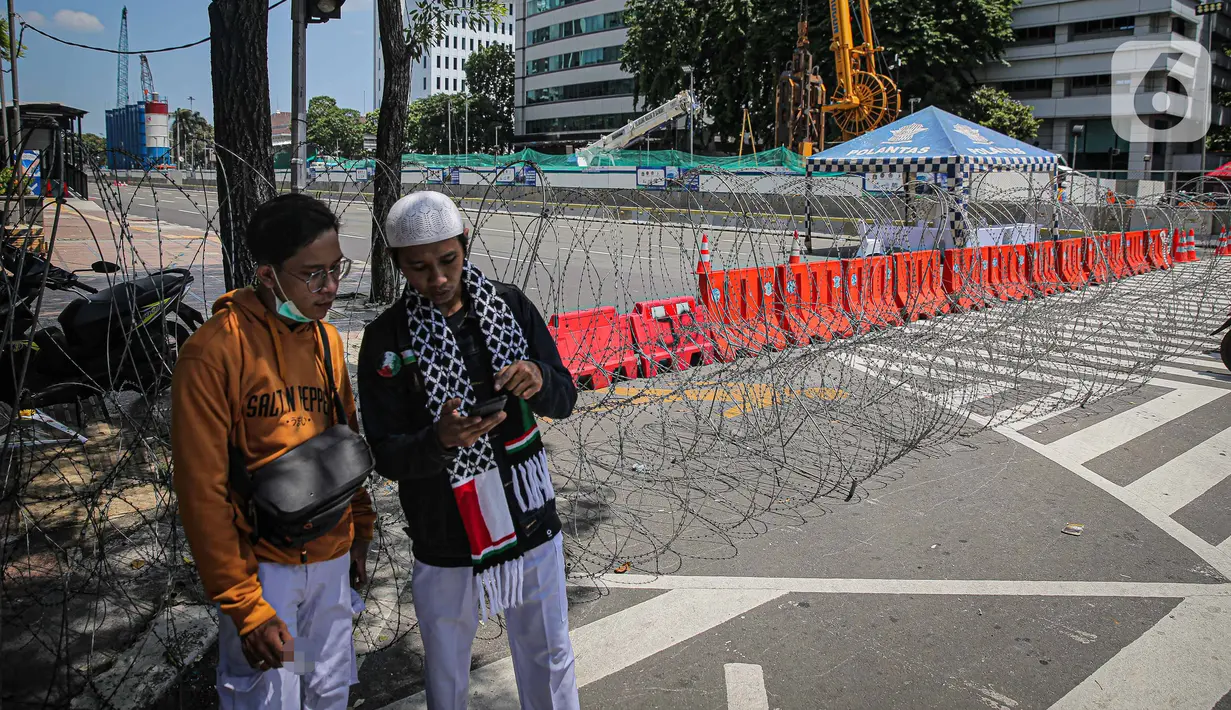 Warga berada dekat kawat berduri di kawasan Jalan MH Thamrin, Jakarta, Kamis (2/12/2021). Polda Metro Jaya memasang barikade di sejumlah titik menuju kawasan Patung Kuda-Monumen Nasional (Monas) Jakarta Pusat guna mengantisipasi kerumunan massa aksi Reuni 212. (Liputan6.com/Faizal Fanani)