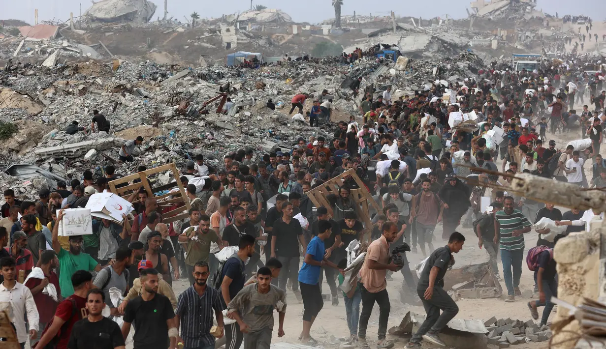 Orang-orang membawa bantuan berjalan di sepanjang jalan al-Rashid di Jabalia barat pada 22 Juni 2025, setelah truk bantuan kemanusiaan memasuki Jalur Gaza utara melalui perbatasan Zikim yang dikuasai Israel, di tengah perang yang sedang berlangsung antara Israel dan Hamas. (Omar AL-QATTAA/AFP)