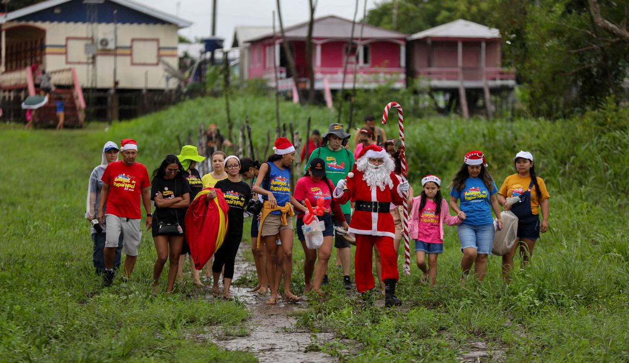 Relawan Jorge Alberto Barrozo, yang mengenakan kostum Sinterklas, berjalan untuk mengantarkan hadiah kepada anak-anak di komunitas tepi sungai di daerah pedesaan Careiro da Varzea, negara bagian Amazonas, Brasil pada Sabtu 20 Desember 2025. (Michael DANTAS/AFP)