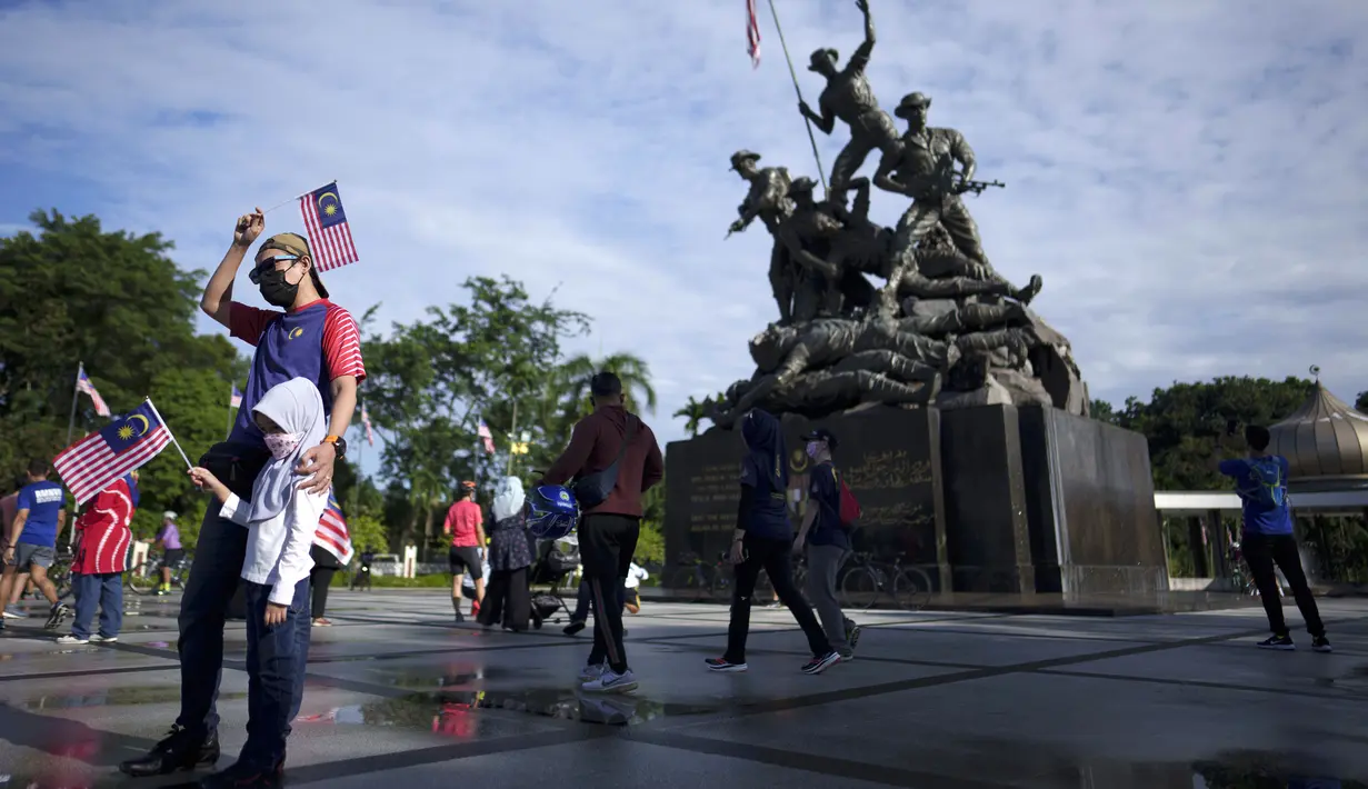 Pengunjung berpose sambil membawa bendera Malaysia di depan Monumen Nasional saat perayaan Hari Nasional ke-64 untuk memperingati kemerdekaan dari penjajahan Inggris di Kuala Lumpur, Malaysia, Selasa (31/8/2021). (AP Photo/Vincent Thian)