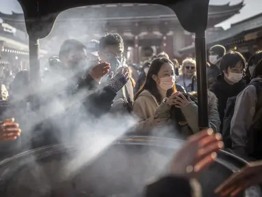 Orang-orang berdoa di sekitar pembakar dupa di kuil Sensoji menjelang liburan Tahun Baru di Tokyo pada 30 Desember 2022. Kuil Sensoji dikenal sebagai tempat wisata paling terkenal di Tokyo. (AFP/Yuichi Yamazaki)