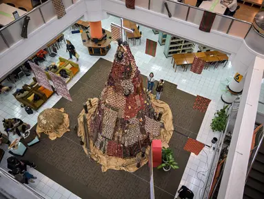 Salah satu mahasiswa berdiri di samping instalasi dekorasi berbentuk pohon Natal dengan motif budaya Papua di Perpustakaan Petra Christian University (PCU), Surabaya, Jawa Timur, Kamis 18 Desember 2025. Jelang perayaan Natal 2025, perpustakaan Petra Christian University (PCU) kembali menghadirkan instalasi dekorasi Pohon Natal tematik. (JUNI KRISWANTO/AFP)