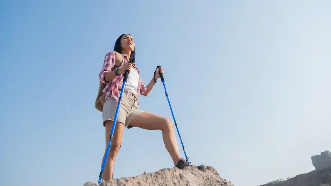 Seorang perempuan berdiri di atas sebuah gunung dengan memegang dua tongkat tracking (Foto Dok: Freepik/jcomp)