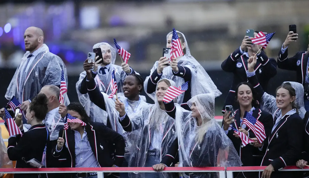 Meskipun hujan deras, semangat para atlet tetap tinggi untuk terus mengikuti upacara pembukaan dengan mengenakan jas hujan bening yang menutupi busana parade mereka.  (AP Photo/Kirsty Wigglesworth)