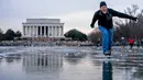 Lincoln Memorial terlihat saat Dan DeMocker dari Tacoma Park meluncurkan bongkahan es ke arah keluarganya saat ia berseluncur es di Reflecting Pool yang membeku di National Mall, Washington, Amerika Serikat, 26 Desember 2022. Selama akhir pekan, suhu beku menggoda banyak orang untuk bermain di Reflecting Pool. (AP Photo/Andrew Harnik)