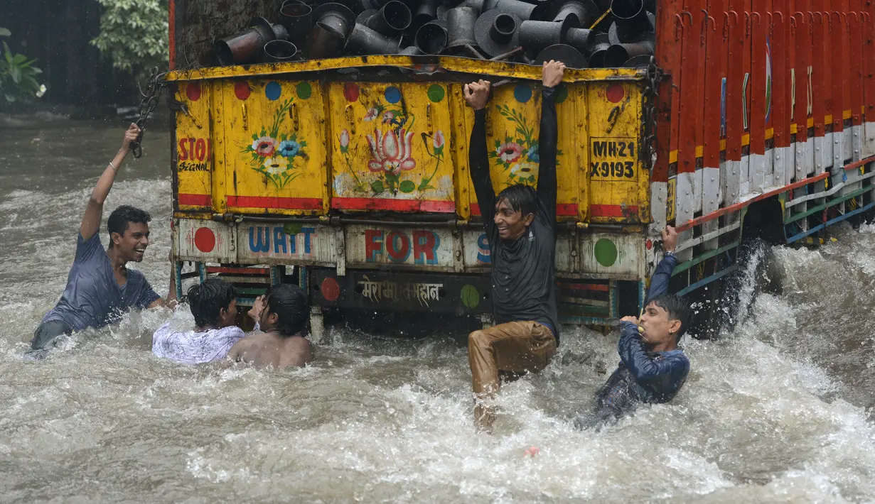Sejumlah Pemuda India bergelantungan di truk saat melintasi banjir selama hujan deras di Mumbai (9/7). Mumbai dan daerah pinggiran lainnya telah mengalami hujan lebat semalaman yang mengakibatkan banjir. (AFP Photo/Punit Paranjpe)