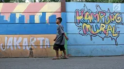 Seorang anak kecil berjalan di sisi tembok yang terdapat lukisan mural di kawasan Kramat Jati, Jakarta, Rabu (4/4). Mural yang ada di tempat ini mencerminkan pesan-pesan sosial positif kepada masyarakat. (Liputan6.com/Herman Zakharia)