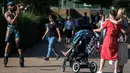 Seorang skater roller berhenti untuk mengambil foto dua wanita saat suhu musim panas mencapai sekitar 28 derajat di Hyde Park di London, Inggris (5/7). (AFP Photo/Chris J Ratcliffe)