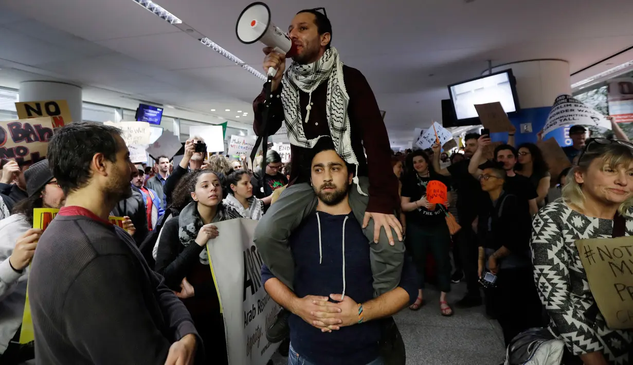 Pengunjuk rasa berorasi di Bandara Internasional San Francisco, Sabtu (28/1). Mereka berunjuk rasa memprotes kebijakan Presiden AS, Donald Trump yang melarang warga dari 7 negara muslim masuk Amerika Serikat. (AP Photo/Marcio Jose Sanchez)