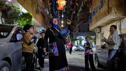 Tradisi yang berlangsung sejak era Abbasiyah ini menjadi simbol kepedulian sosial, sering kali menyerukan doa atau nama warga, sekaligus menjaga suasana Ramadan tetap khidmat. Tampak dalam foto, Dalal, seorang wanita Mesir yang dikenal sebagai 'musaharati', berjalan di sepanjang jalan sambil memukul gendang dan menyerukan umat Muslim untuk bangun dan makan sahur selama bulan suci Ramadan di distrik Hadayek el-Maadi, selatan Kairo pada Minggu 1 Maret 2026. (Khaled DESOUKI/AFP)