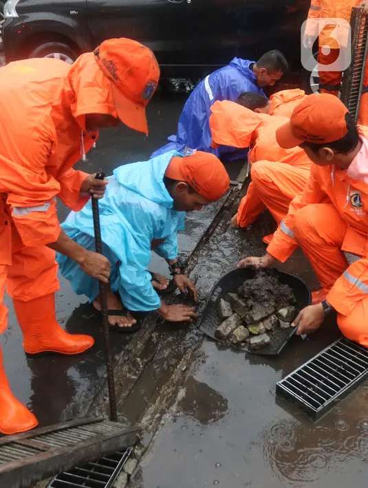 Petugas Penanganan Prasarana dan Sarana Umum (PPSU) membersihkan saluran air di kawasan Gelora Bung Karno, Jakarta, Selasa (17/12/2019). Petugas PPSU membersikan saluran air saat terjadi genangan usai hujan deras mengguyur Jakarta. (Liputan6.com/Herman Zakharia)