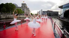 Penari dari Berlin State Ballet menari "Swan Lake" di atas kapal pesiar selama tur pusat kota saat kapal berlayar di depan gedung Reichstag (kiri), Berlin, Jerman, Kamis (10/6/2021). Pertunjukan diikuti oleh banyak orang di sepanjang rute. (Christoph Soeder/dpa via AP)