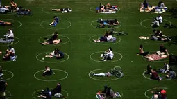 Orang-orang berusaha menjaga jarak dalam lingkaran putih saat bersantai di Domino Park, Brooklyn di Kota New York, Minggu (17/5/2020). Pengunjung taman berjemur dengan tetap menerapkan protokol penularan coorna Covid-19. (Photo by Johannes EISELE / AFP)