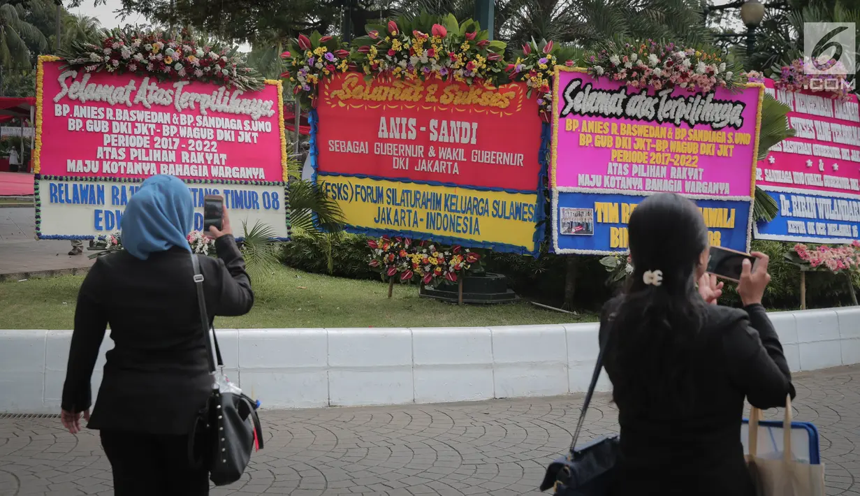 Sejumlah orang menggunakan ponselnya mengambil gambar karangan bunga ucapan selamat atas pelantikan Gubernur dan Wakil Gubernur DKI terpilih, Anies Baswedan dan Sandiaga Uno di Halaman Balai Kota DKI Jakarta, Senin (16/10). (Liputan6.com/Faizal Fanani)