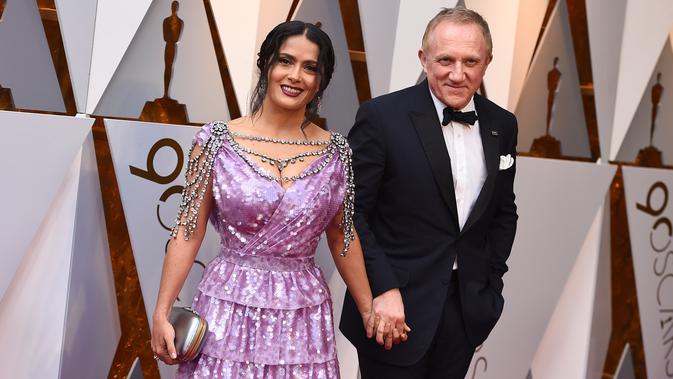 Salma Hayek dan suami, Francois-Henri Pinault menghadiri karpet merah Piala Oscar 2018 di Los Angeles, Minggu (4/3). Tambahan aksesori seperti clutch silver dan anting chandeliernya pun membuat tampilan Salma cukup stunning. (Jordan Strauss/Invision/AP)