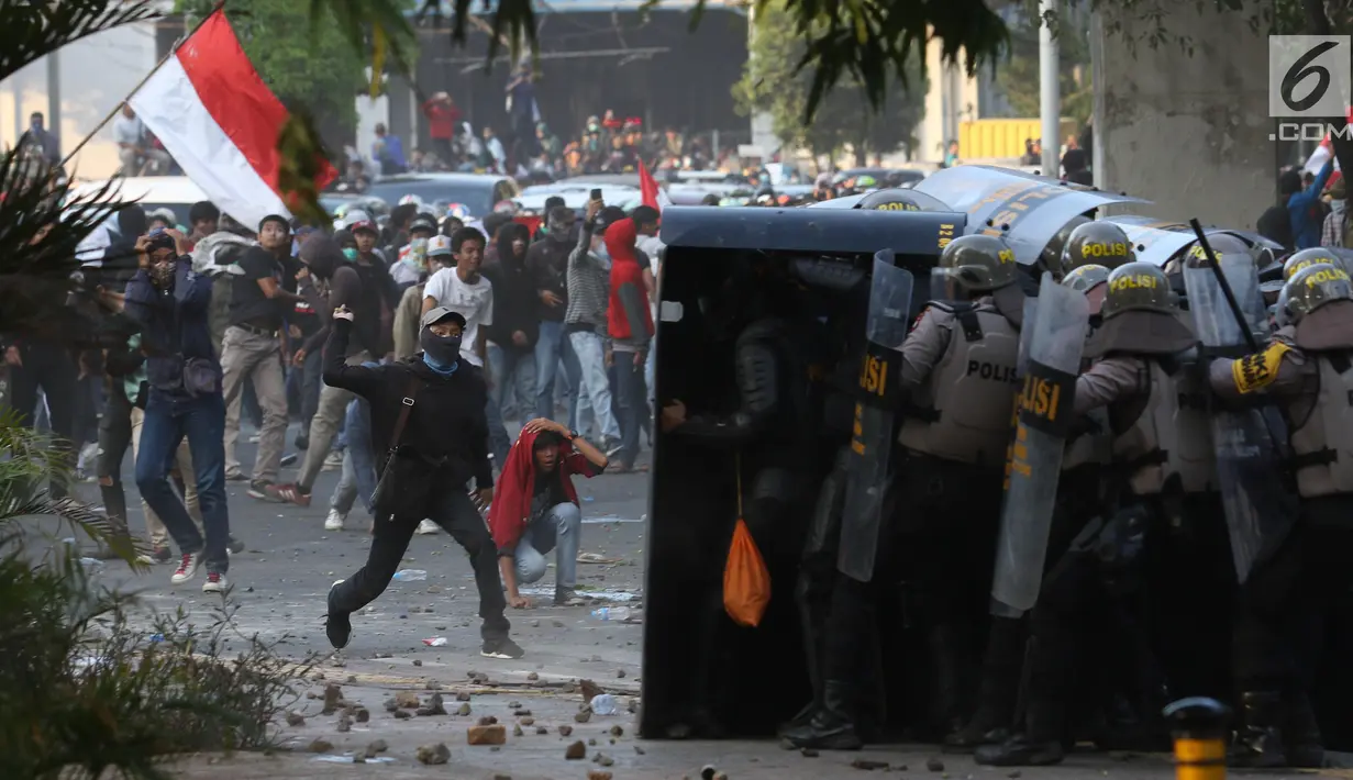 Massa melempar batu ke arah polisi yang membentuk barikade dengan tameng di sekitaran Gedung DPR RI, Jakarta, Senin (30/9/2019). Kericuhan pecah lantaran massa yang kebayakan terdiri dari pelajar tersebut berusaha masuk ke area depan DPR. (Liputan6.com/Angga Yuniar)