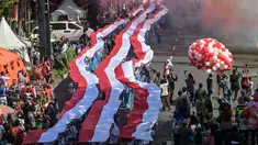 Para siswa dari berbagai sekolah membentangkan bendera Merah Putih panjang saat berbaris di jalan-jalan selama acara upacara untuk memperingati HUT ke-80 Kemerdekaan Indonesia di Surabaya, Jawa Timur pada 17 Agustus 2025. (Juni KRISWANTO/AFP)