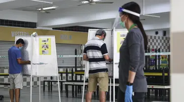 Para pemilih mengenakan masker saat memberikan suara dalam pemilu di TPS Sekolah Tinggi Chung Cheng, Singapura, Jumat (10/7/2020). Pemilu di tengah pandemi COVID-19, warga Singapura memberikan suara mereka dengan mengenakan masker dan sarung tangan plastik. (AP Photo)