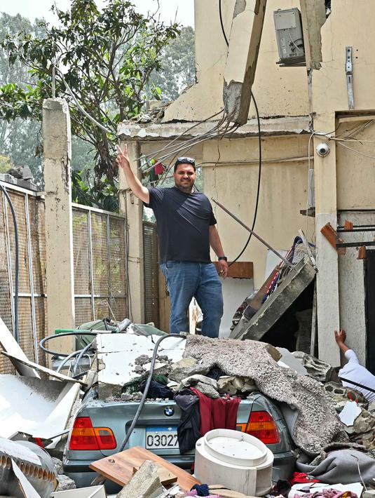 Mereka mulai berbenah membersihkan puing-puing, dan memeriksa kerusakan tempat tinggal. Tampak dalam foto, seorang warga mengacungkan tanda kemenangan sambil berdiri di atas mobil yang rusak dan puing-puing rumah yang hancur saat kembali ke kota Nabatieh, Lebanon Selatan pada Sabtu 18 April 2026. (FADEL itani/AFP)