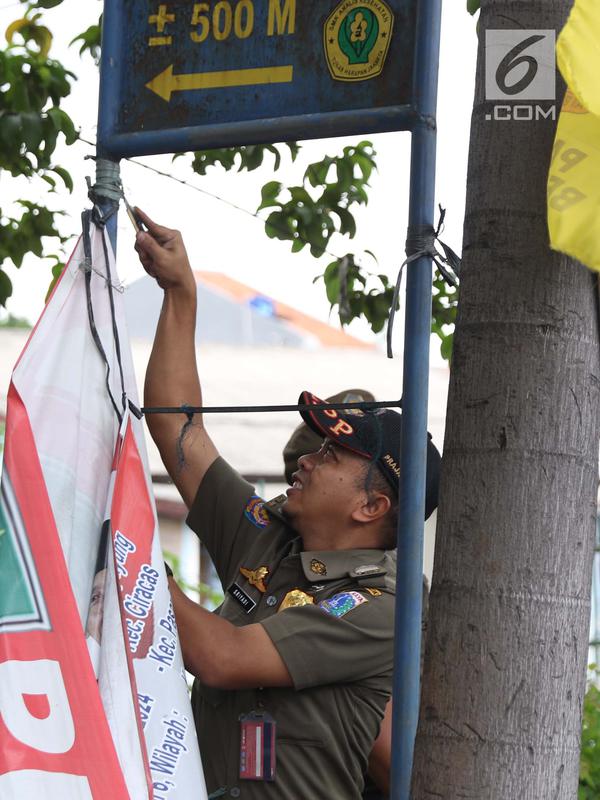 Petugas Satpol PP menurunkan APK yang terpasang di Jalan Raya Bogor dekat GOR Ciracas, Jakarta, Rabu (23/1). Penurunan APK ini karena pemasangannya dianggap melanggar ketentuan. (Liputan6.com/Helmi Fithriansyah)