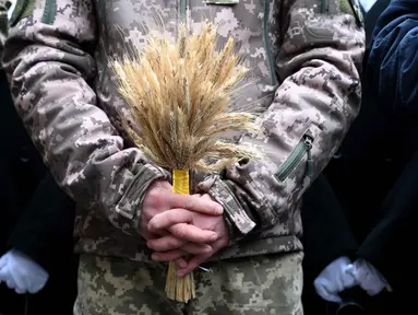 Seorang tentara Ukraina memegang hiasan tradisional Natal 'Didukh' saat ikut serta dalam prosesi Malam Natal di Lviv pada 24 Desember 2025. Di tengah ancaman invasi Rusia, warga Ukraina bersukacita menyambut perayaan Natal 2025. (YURIY DYACHYSHYN/AFP)