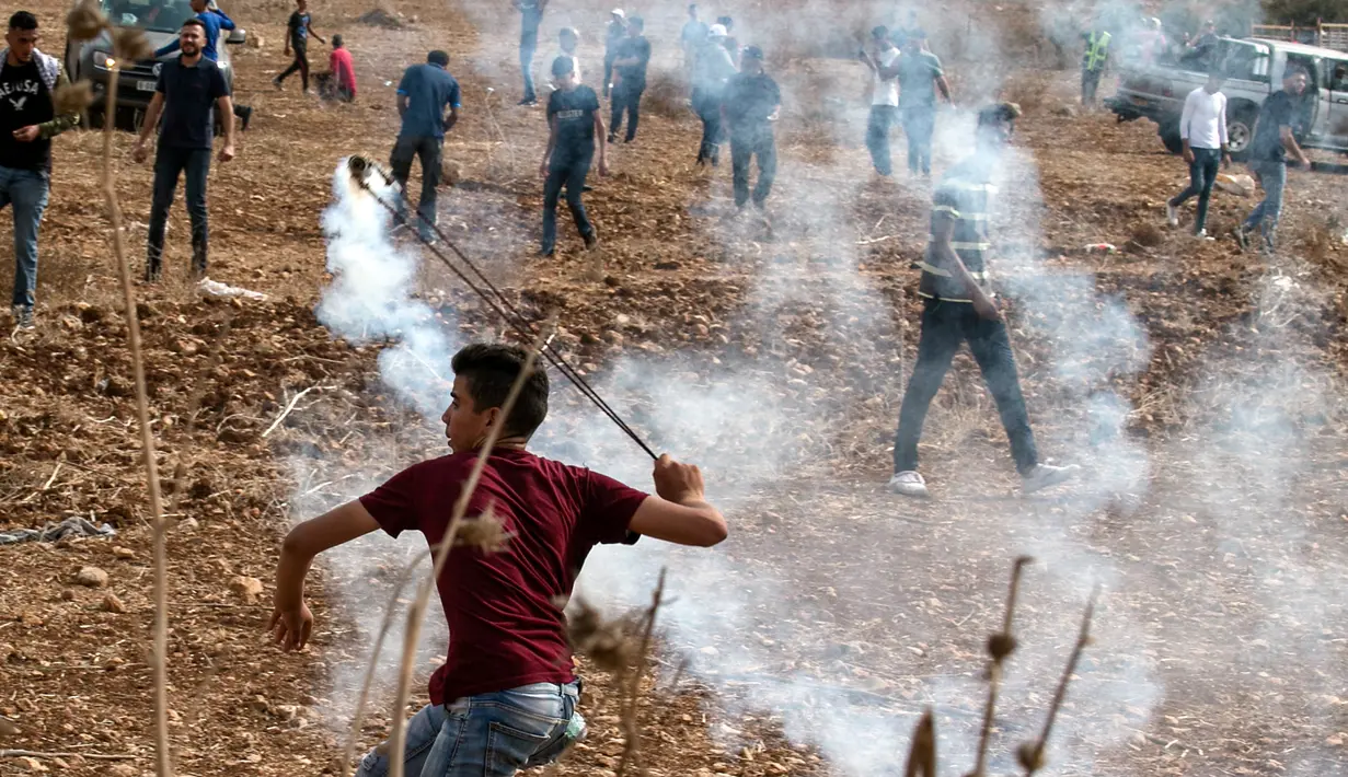 Pengunjuk rasa Palestina menggunakan katapel untuk melemparkan kembali granat gas air mata ke pasukan keamanan Israel saat demonstrasi menentang pembangunan pos terdepan Israel di desa Palestina, Ramallah, Tepi Barat, Kamis (17/10/2019). (JAAFAR ASHTIYEH/AFP)