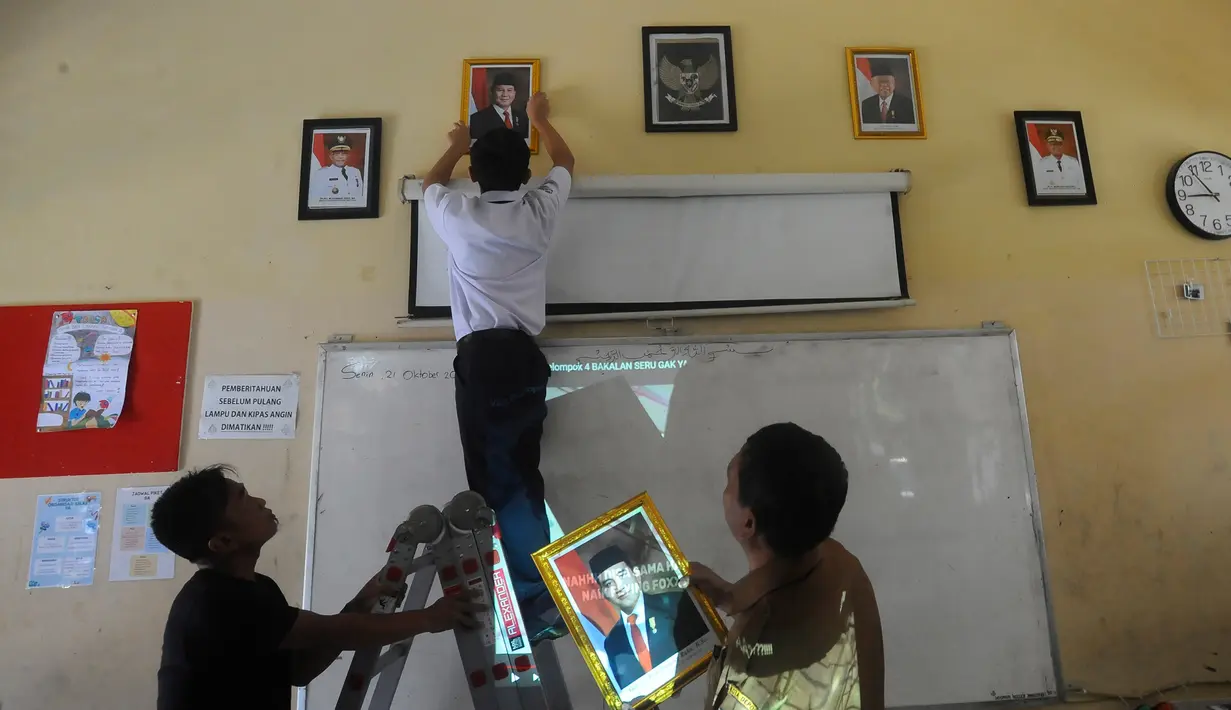 Murid kelas IX SMPN 2 Depok memasang pigura bergambar foto Presiden Republik Indonesia Prabowo Subianto untuk menggantikan foto Presiden ke-tujuh Joko Widodo di alah satu kelas, Jawa Barat, Senin (21/10/2024). (merdeka.com/Arie Basuki)