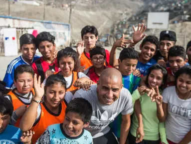 Mantan pemain bola Juventus, David Trezeguet berfoto bersama anak-anak di komunitas San Pablo Mirador, Peru (13/7). Trezeguet melakukan kunjungan ke Peru untuk mempromosikan Paris yang menjadi tuan rumah Olimpiade 2024. (AFP Photo/Ernesto Benavides)